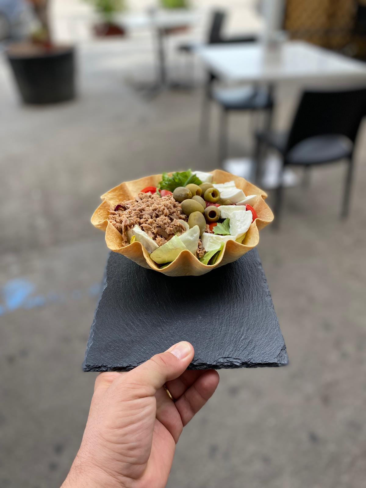 A hand holding a slate board with a tuna, olive and mozzarella basket on it