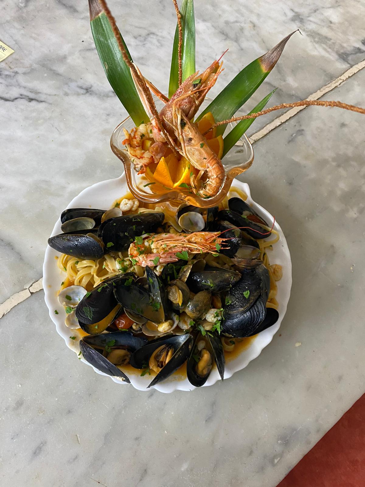 Linguine with mussels, clams and prawns on a scalloped plate on a marble table